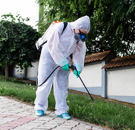 Employee wearing protective equipment while spraying lawn
